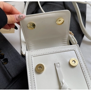 Detail of white leather shoulder bag featuring dual gold magnetic closures and stitching