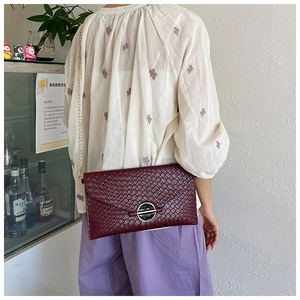 Close-up of burgundy woven leather bag with a round metal buckle and gold chain strap