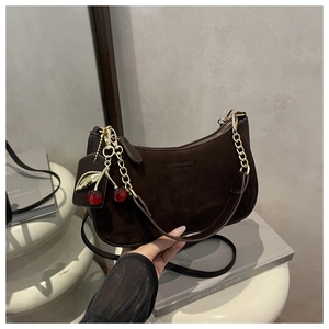 Close-up of brown suede hobo bag with gold chain and red cherry charm detail