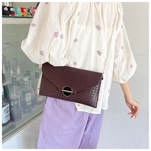 Detail of a dark reddish brown woven envelope bag with a round gold metallic lock