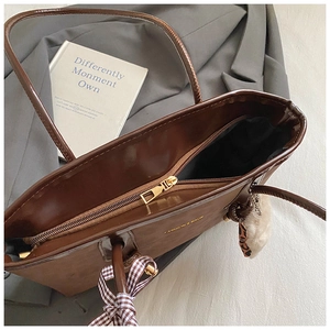 Dettaglio borsa tote marrone lucida con cerniera dorata e ciondolo decorativo in peluche