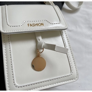 Detail of white PU leather crossbody bag with gold FASHION text and metal pendant