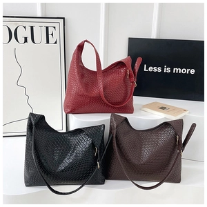Three woven leather tote bags in burgundy, black and brown on a minimalist display