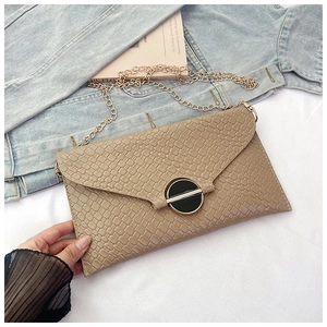 Detail of elegant beige woven envelope bag with gold chain strap and metal buckle