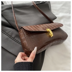 Detailed shot of brown crocodile embossed baguette bag with golden metal buckle