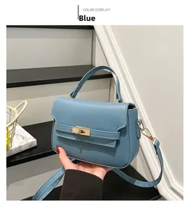 Blue PU leather handbag with golden twist lock and top handle held by hand