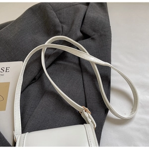 Detailed close-up of white leather square bag with adjustable shoulder strap on a grey suit
