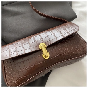 Detail of crocodile embossed brown shoulder bag featuring a sleek gold capsule clasp