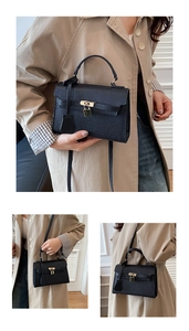 Detail of black lychee leather handbag with gold hardware lock and adjustable shoulder strap