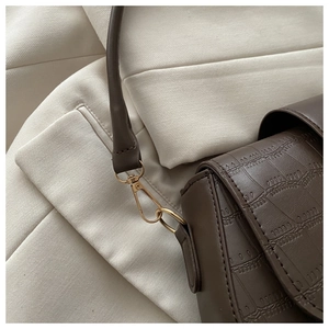 Close-up of deep brown crocodile embossed leather texture with gold metal buckle detail