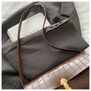 Detail of dark brown croc-effect shoulder bag with a gold twist lock on a white book