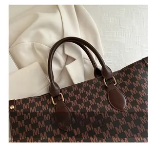 Close-up of brown tote bag with M-letter pattern and golden hardware connectors