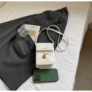 Detail of white minimalist mini crossbody bag with leather strap and metal pendant on grey suit