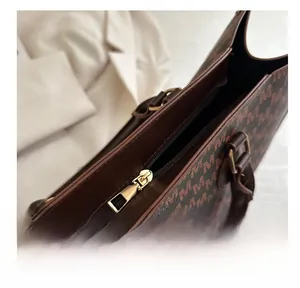Detail view of smooth metal zipper and monogram pattern on brown leather tote bag