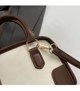 Detail of gold hardware and leather strap attachment on a beige and brown shoulder bag