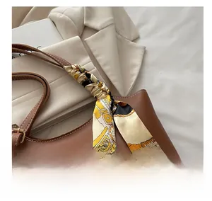 Close-up of brown leather tote bag handle wrapped with a decorative patterned silk scarf