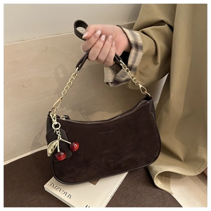 Detail of dark brown suede shoulder bag with gold chain and red cherry charm