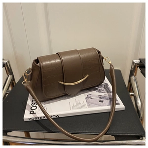 Close-up of crocodile embossed leather texture and crescent golden buckle on a dark brown bag