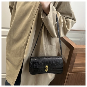 Detail of a black crocodile-embossed underarm bag with gold metal clasp on a model