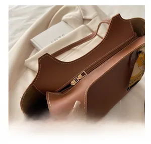 Detail view of smooth metal zipper and white contrast stitching on a brown leather tote bag