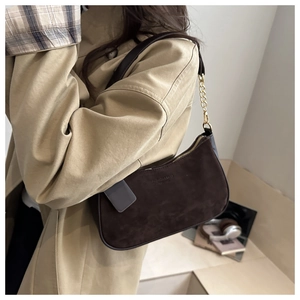 Detail of dark brown suede crescent shoulder bag with gold chain strap on model
