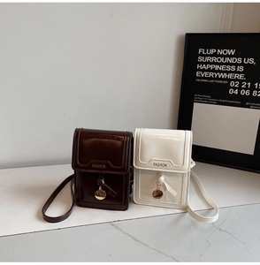 Detail of glossy brown and cream shoulder bag with FASHION logo and gold metal pendant