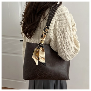 Close-up of a vintage brown tote bag with a silk scarf tied on the handle