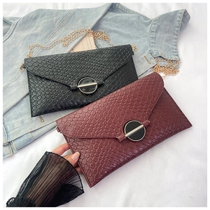 Detail of woven texture envelope bag with gold chain strap and decorative round buckle