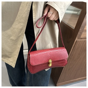 Detail of red crocodile textured leather shoulder bag with gold metal buckle closure