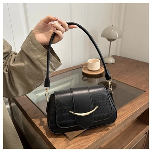 Detail of black faux crocodile leather shoulder bag with golden metallic curved clasp