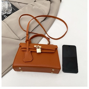 Detailed view of brown lychee grain leather handbag with gold lock and size reference phone