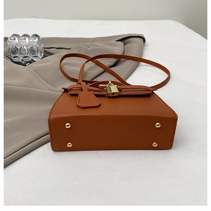 Detail of caramel pebbled leather handbag featuring gold hardware and protective feet