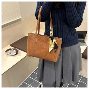 Détail d'un sac cabas en cuir marron avec un foulard décoratif noué à la poignée