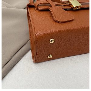 Macro view of brown lychee grain leather handbag with gold hardware and stitching