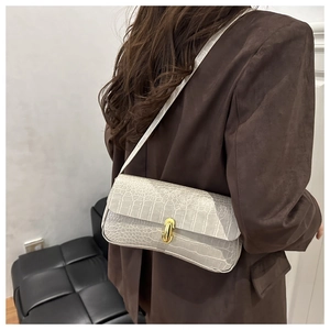 Detail of light beige baguette bag with crocodile texture and gold clasp on shoulder