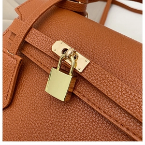 Macro view of gold-tone hardware padlock on brown lychee texture leather handbag
