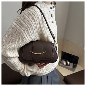 Side view of dark brown crocodile pattern shoulder bag with a gold crescent metal buckle