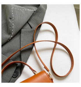Dettaglio della tracolla in pelle color caramello con cuciture fini su un blazer grigio