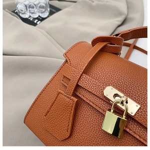 Macro detail of brown pebble leather handbag featuring a golden lock and strap
