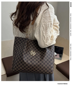 Close-up of brown tote bag with M letter print and gold chain strap on shoulder