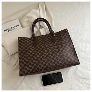 Detail of large tote bag with M-pattern print and leather handles on beige blazer