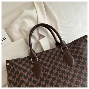 Detail of a brown tote bag featuring M-print pattern, leather handles and gold metal hooks