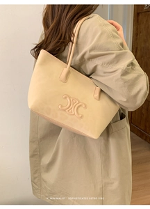 Minimalist beige tote bag featuring an embossed logo and a long shoulder strap on model
