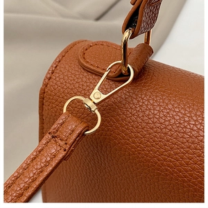 Macro view of brown lychee leather bag featuring gold lobster clasp and fine stitching