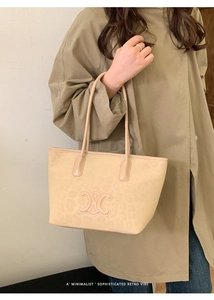 Chic beige leopard print tote bag with metallic emblem worn with a stylish trench coat