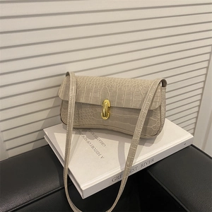 Elegant beige croc-embossed underarm bag with gold capsule clasp on white books