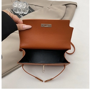 Detail shot of open brown lychee leather handbag with golden lock and black interior lining