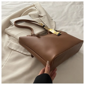 Detail of a brown leather tote bag featuring a decorative printed scarf on the handle