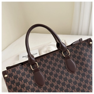 Detail view of the brown leather handle with golden hardware and monogram printed tote