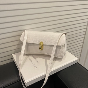 White faux crocodile skin underarm bag with gold metal buckle on a white book